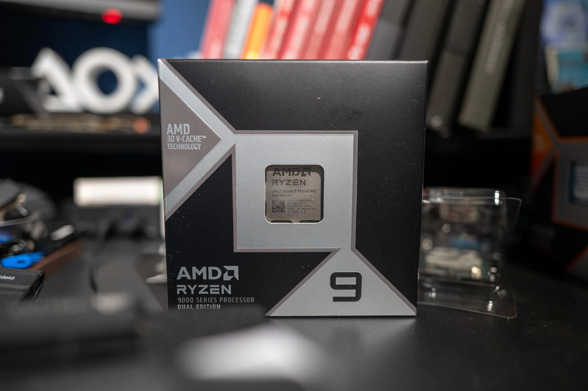 Новый процессор AMD Ryzen 9 9950X3D2 в товарной упаковке на фоне книжной полки 