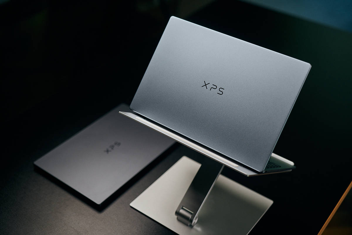 Ноутбук Dell XPS 13 серебристого цвета стоит на подставке, рядом на черном столе лежит такой же ноутбук