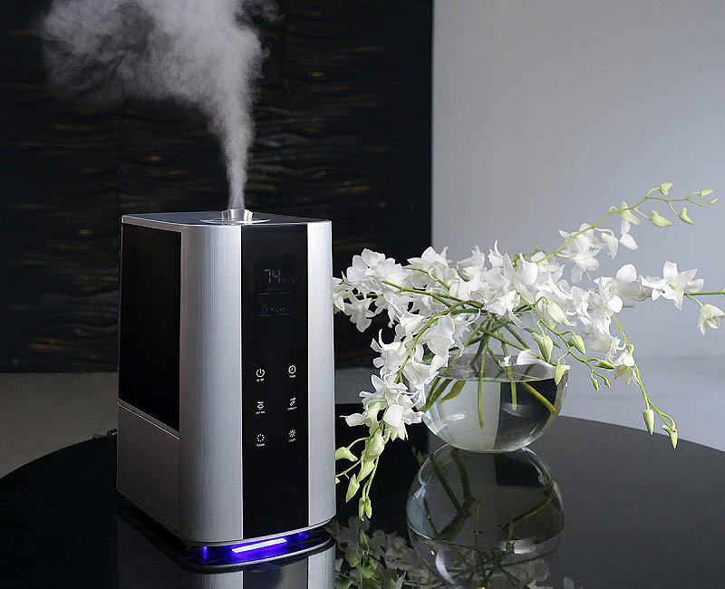 Стильный прямоугольный увлажнитель воздуха на черном столе рядом с цветами.